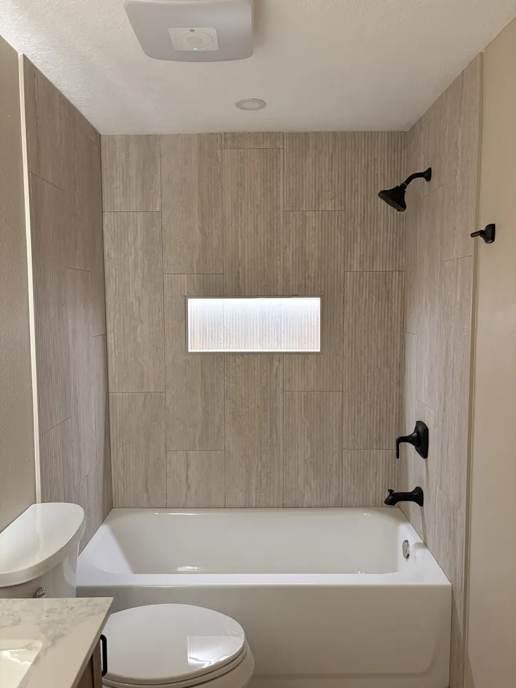 Tub and shower combination with wood-look porcelain tile, a lit shampoo niche and matte black fixtures