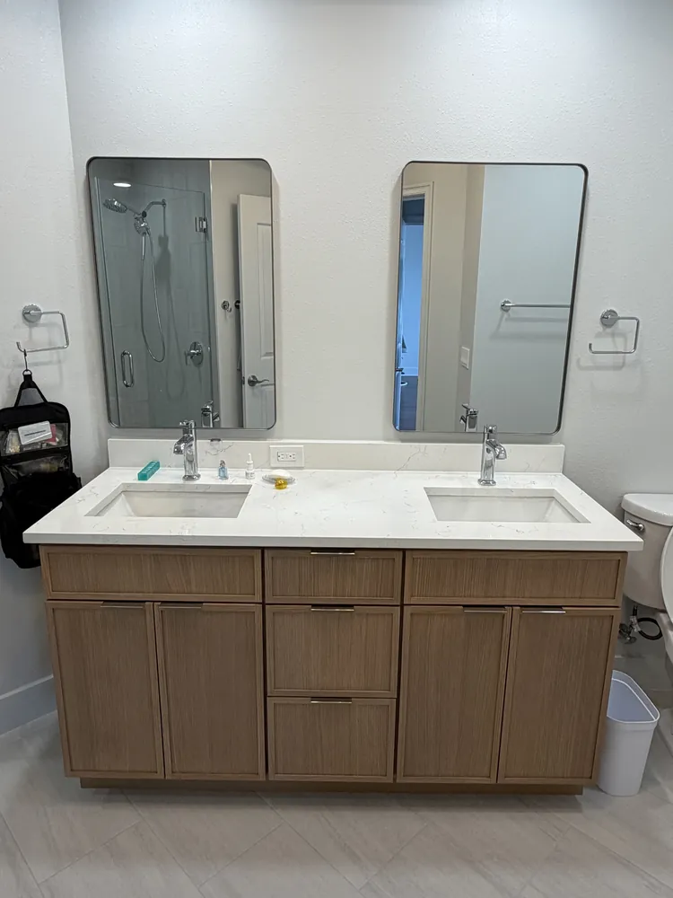 Double vanity in light wood with a white quartz countertop and two frameless mirrors