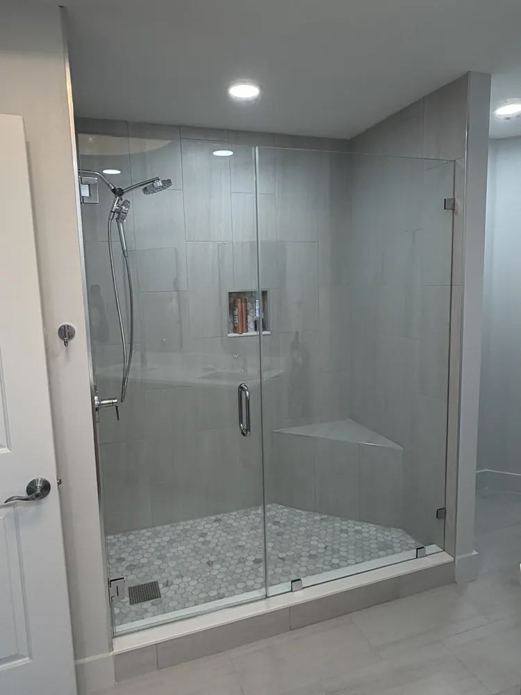 Frameless glass walk-in shower with a built-in bench, tile niche and pebble floor