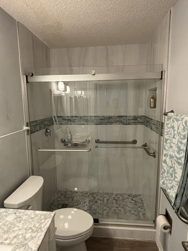 Sliding glass shower with a grey mosaic accent band and two stainless grab bars