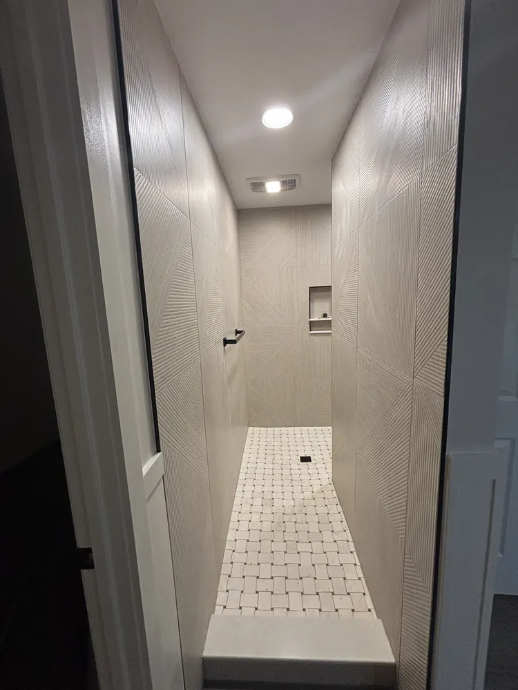 Walk-in shower with textured wall tile, matte black fixtures and a black-and-white mosaic floor