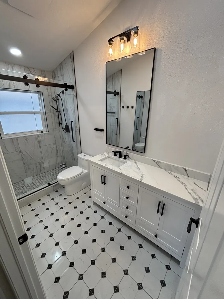 Bathroom with a black-and-white dot tile floor, white vanity, black faucet and a sliding barn-style glass shower door