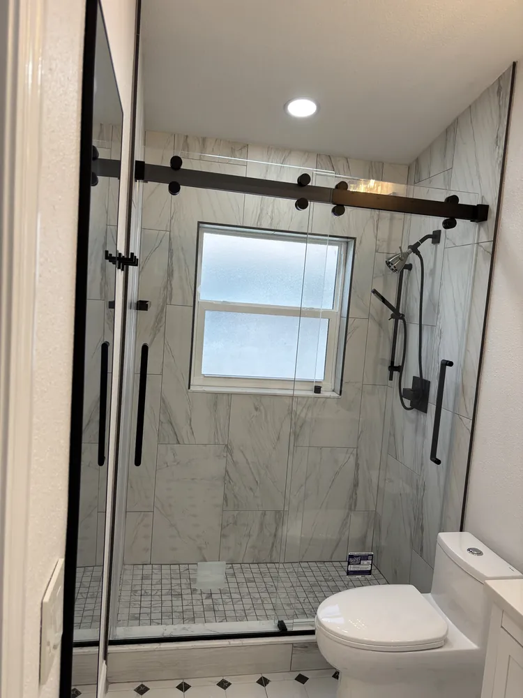 Shower with a barn-style sliding glass door, marble-look tile and a window for natural light