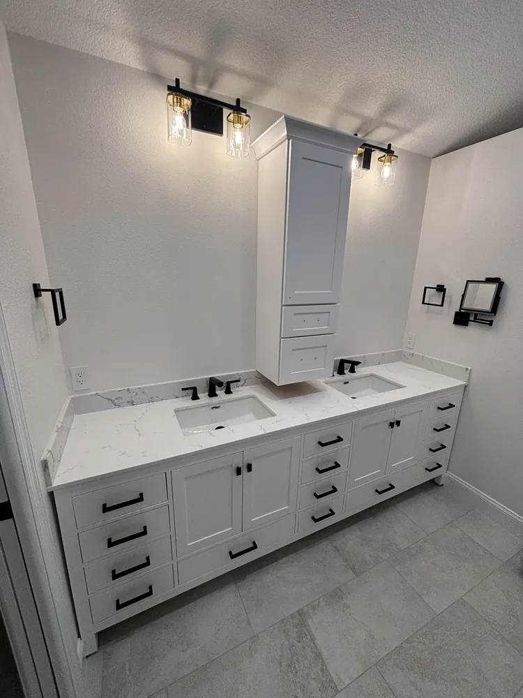 White double vanity with black hardware, black faucets and Edison-bulb sconces over a tall mirror cabinet