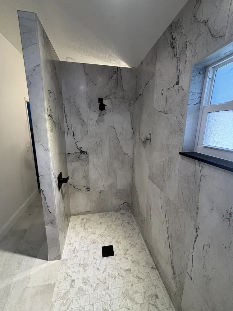 Curbless walk-in shower with large-format marble-look porcelain tile and a black rain shower head
