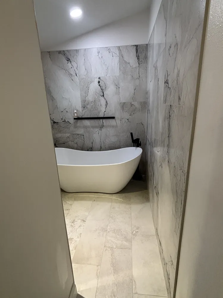 Freestanding soaking tub in a marble-look tiled wet room with a wall-mounted tub filler