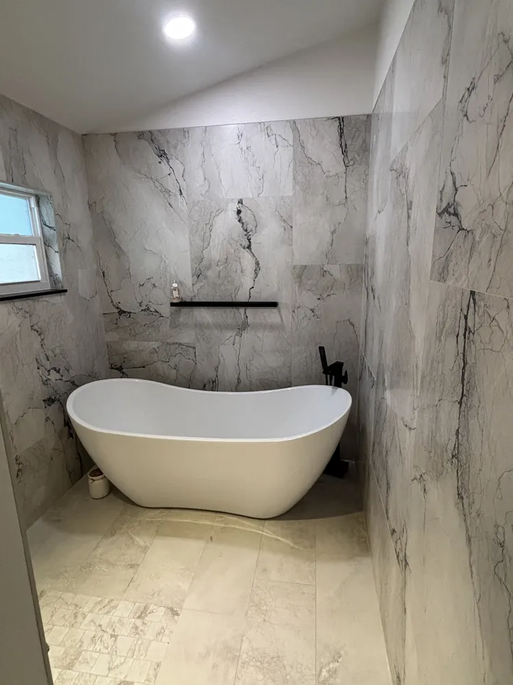 Freestanding white tub against floor-to-ceiling marble-look tile in a remodeled master bath