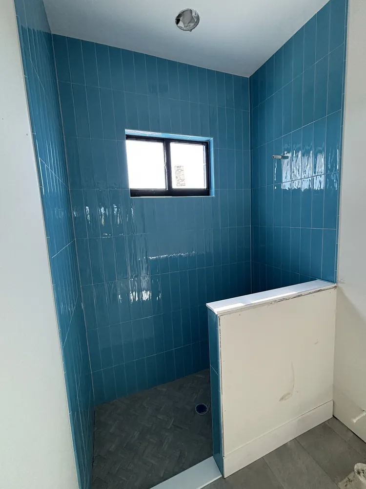 Shower wrapped in glossy blue vertical subway tile with a half wall and grey floor tile