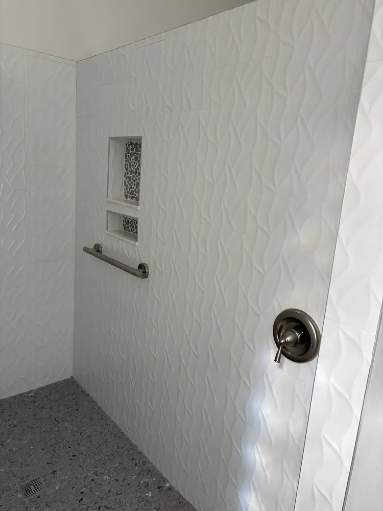 Walk-in shower with white three-dimensional wave tile, a corner niche and terrazzo-look floor