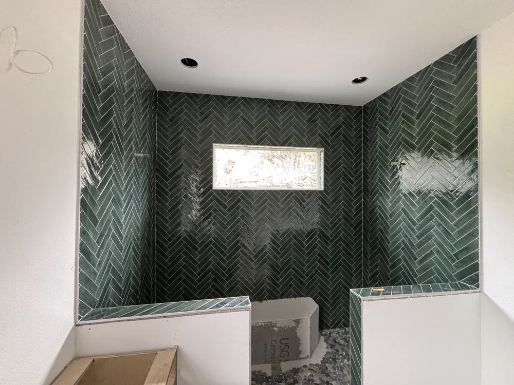 Shower walls in dark green herringbone tile with a window and knee wall during installation