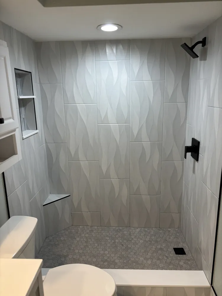 Walk-in shower with grey diamond-pattern tile, a built-in bench and matte black fixtures