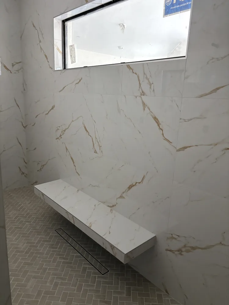 Shower with gold-veined marble-look tile, a floating stone bench and herringbone floor