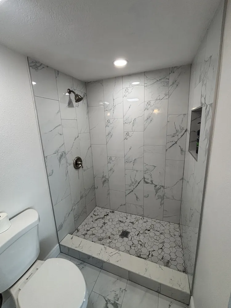 Finished shower with white marble-look tile, a recessed niche and a mosaic floor