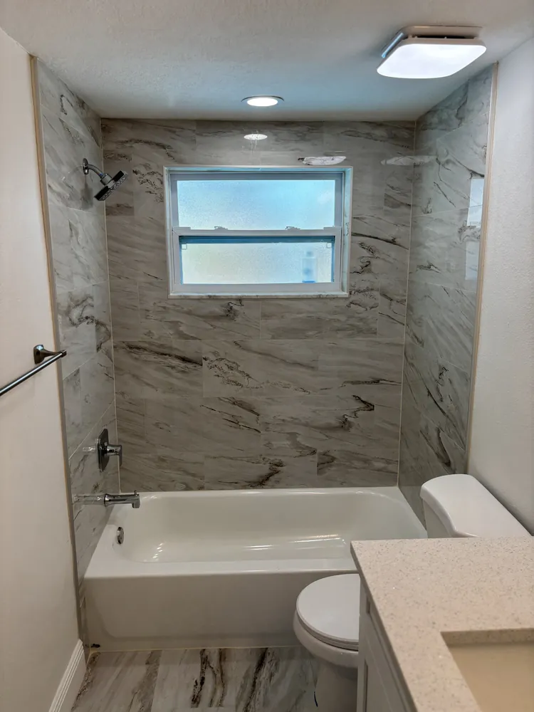 Tub and shower with marble-look wall tile, a window and a new quartz vanity top
