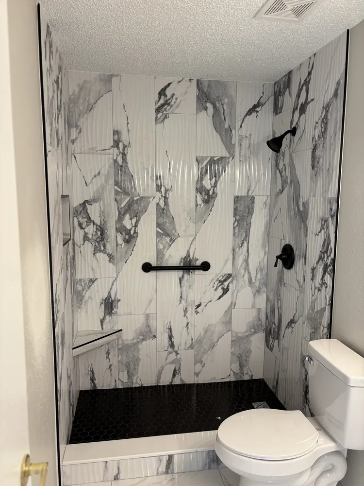 Shower with dramatic grey-and-white marble-look tile, black fixtures and a black mosaic floor