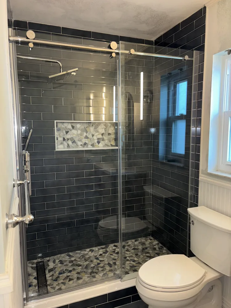 Shower with navy subway tile, a mosaic niche, pebble floor and a sliding glass door
