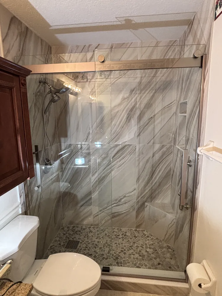 Shower with flowing marble-look tile, pebble floor and a sliding frameless glass door