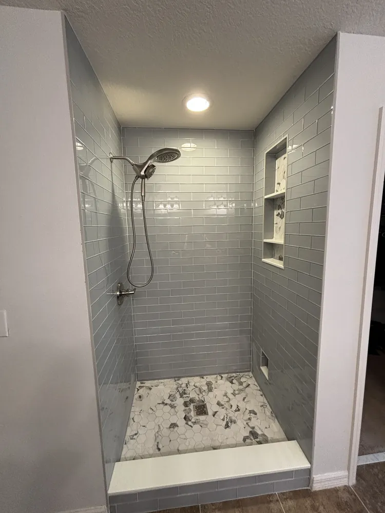 Walk-in shower with grey subway tile, a corner niche and a grey-and-white mosaic floor