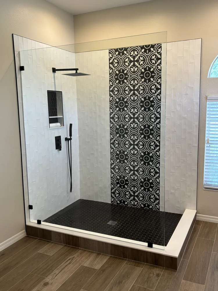 Curbless shower with a black-and-white patterned accent strip, black fixtures and a black mosaic floor