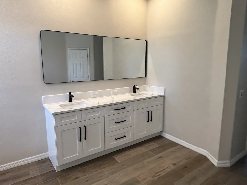 White double vanity with quartz top, black faucets and a wide black-framed mirror