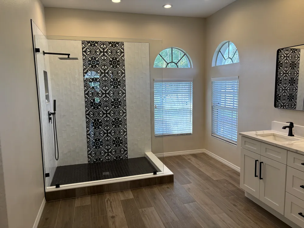 Master bath with a patterned accent shower, arched windows and wood-look plank floor