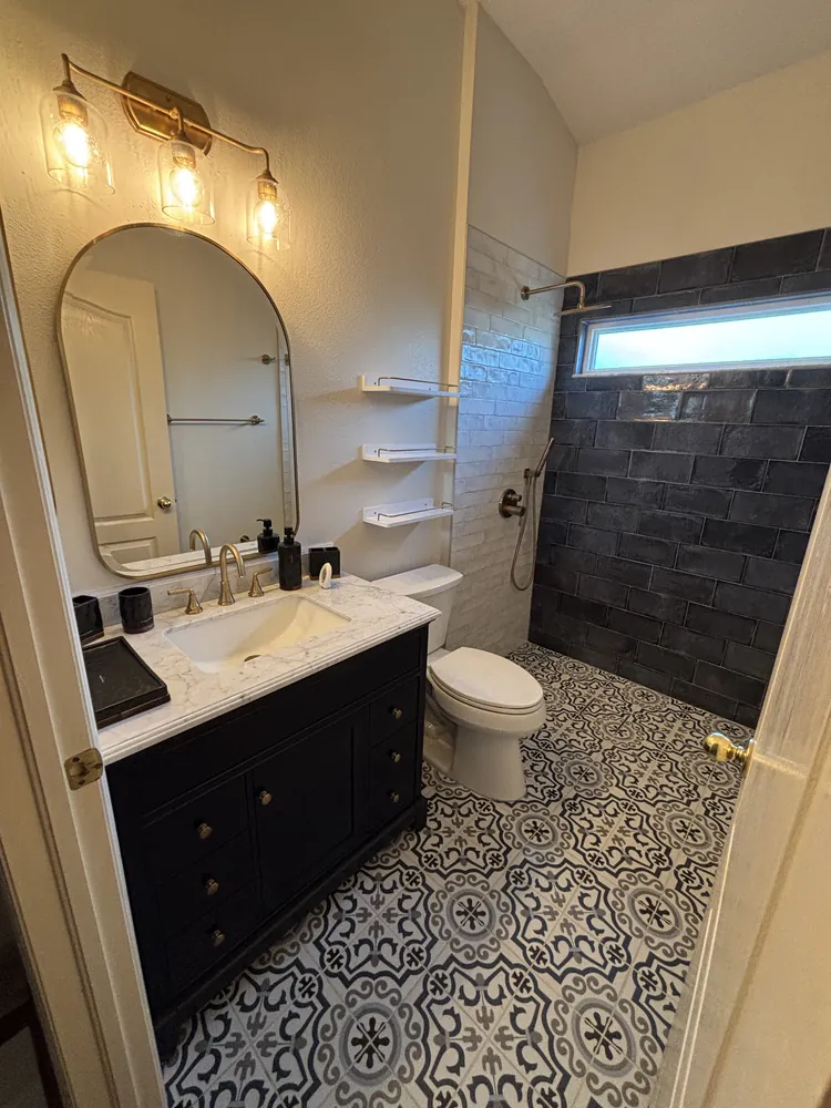 Bathroom with a patterned encaustic-style floor, navy vanity, brass faucet and arched mirror