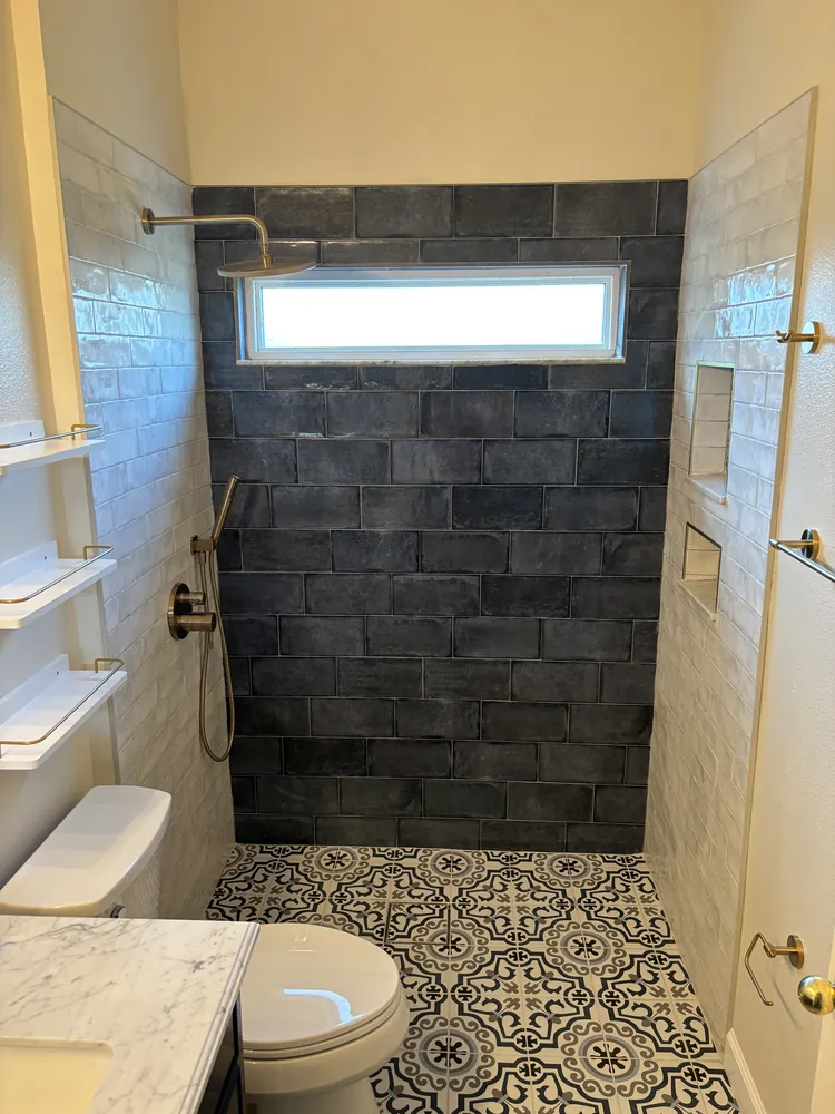 Shower with charcoal subway tile, brass fixtures and a window above the niche