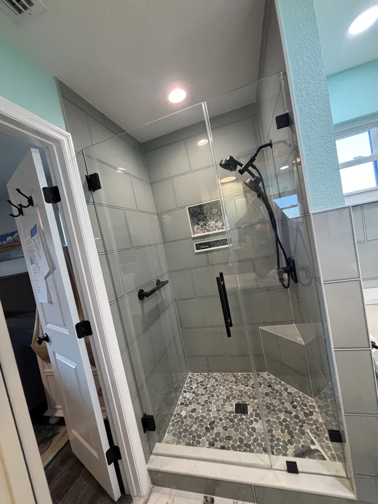 Frameless glass shower with a bench, pebble floor and black fixtures