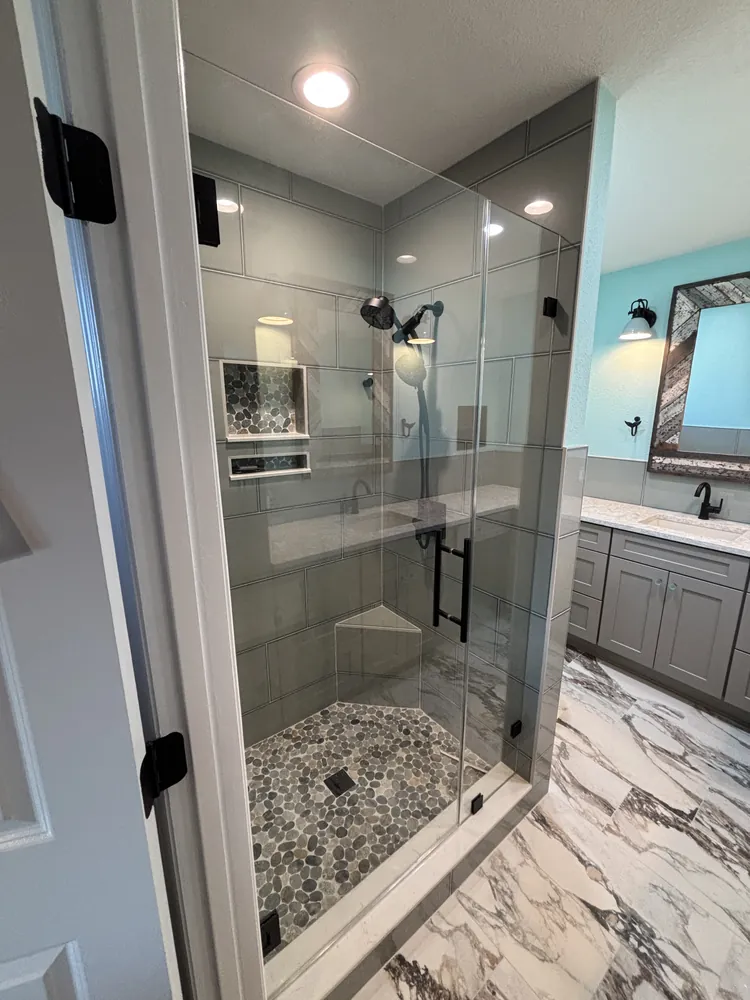 Frameless glass shower beside a grey vanity in a remodeled master bathroom