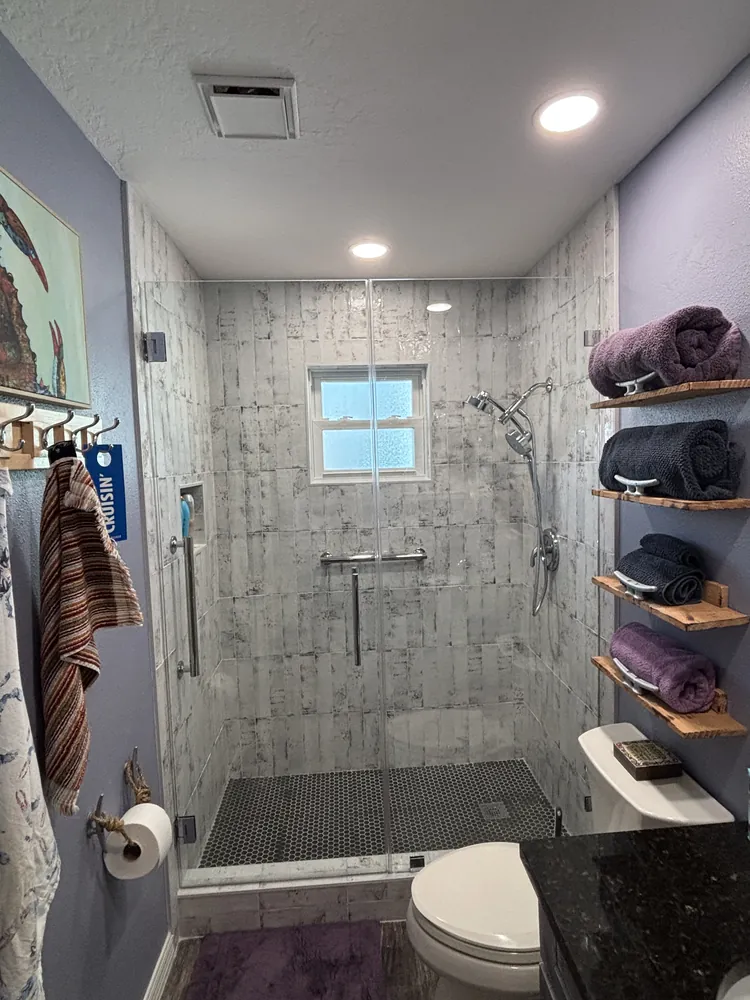 Shower with wood-look tile, floating shelves and a black mosaic floor