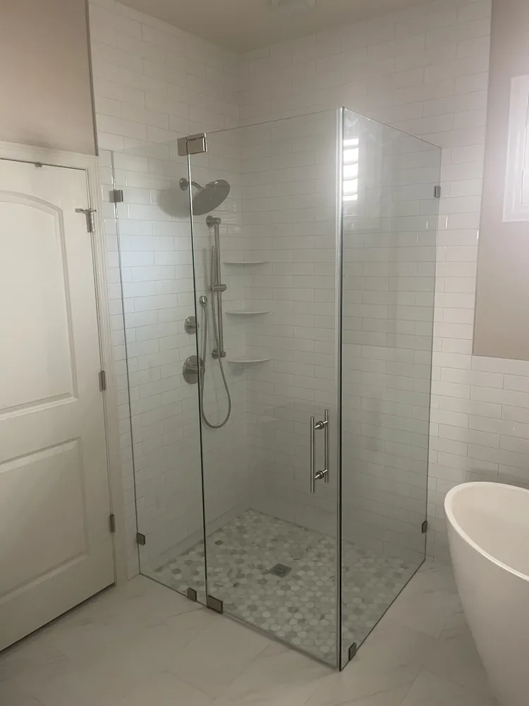 Frameless glass corner shower next to a freestanding tub in a white master bath