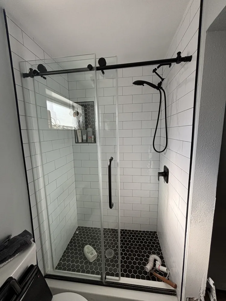 White subway tile shower with a black barn-style glass door and black hexagon floor