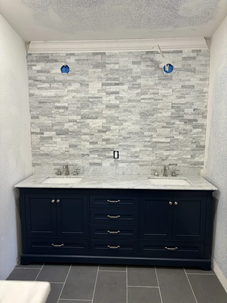 Navy double vanity with a grey stone mosaic backsplash wall and dark floor tile