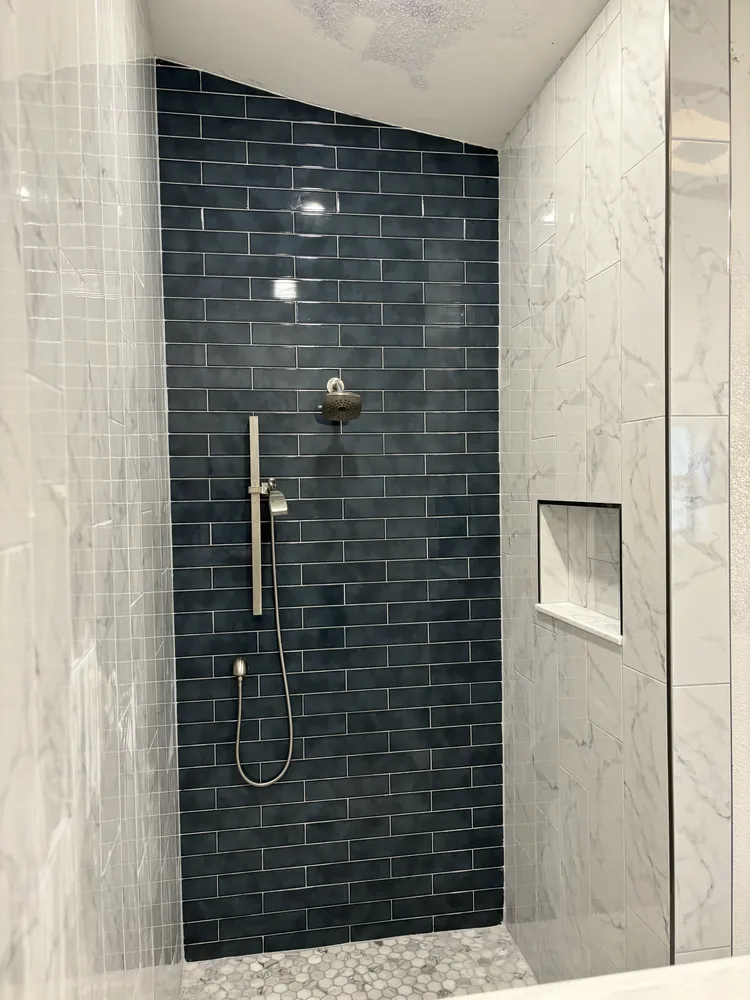 Walk-in shower with a navy subway tile accent wall, marble-look surround and pebble floor