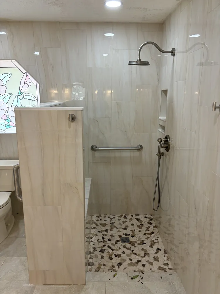 Roll-in accessible shower with grab bars, a bench, hand shower and pebble floor