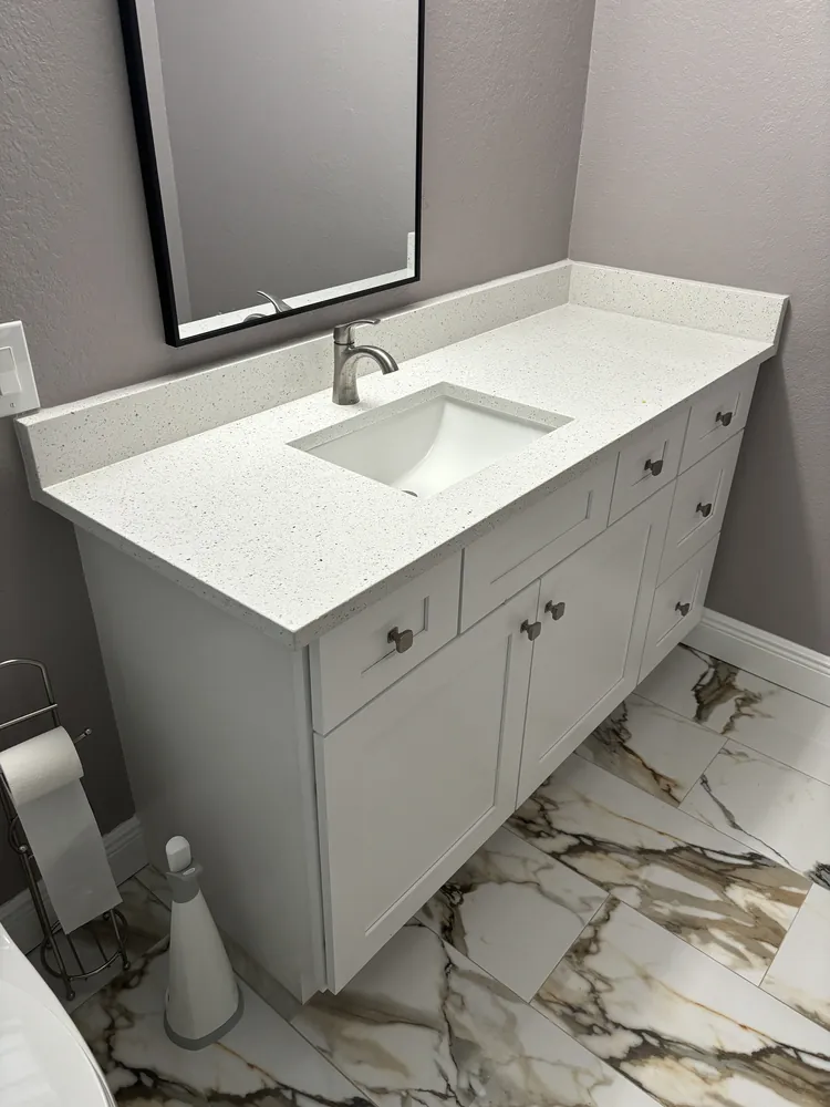 White vanity with speckled quartz top over bold marble-look floor tile
