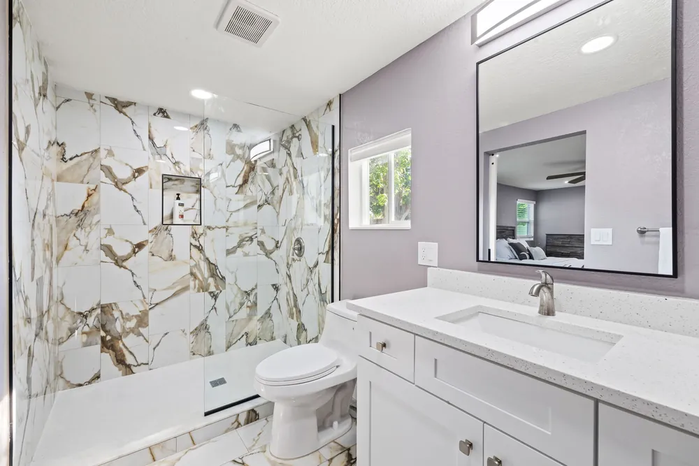 Bathroom with a gold-veined marble-look shower, frameless glass and a white vanity