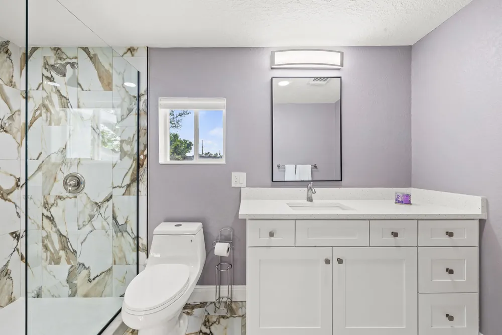 Walk-in shower with gold-veined marble-look tile beside a white shaker vanity