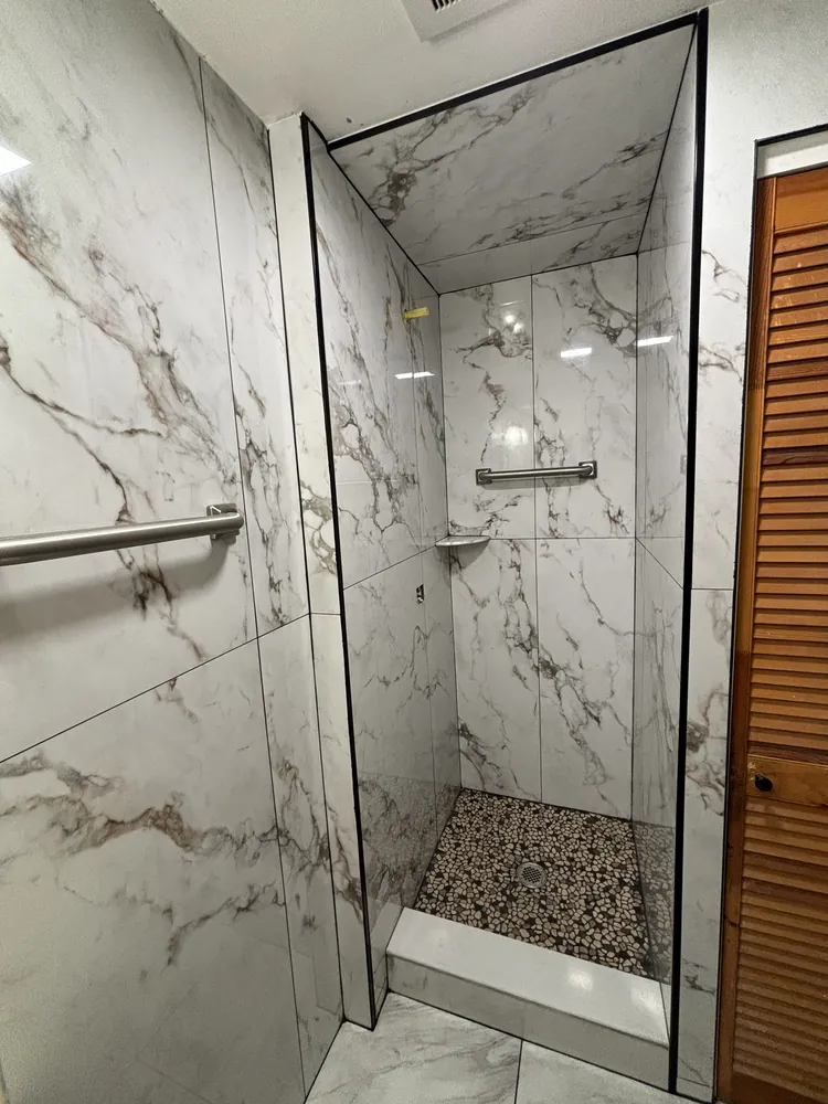 Shower with grey marble-look tile, a window and a pebble mosaic floor
