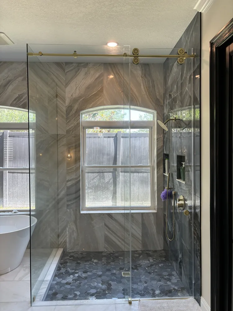 Walk-in shower with a sliding frameless glass door, chevron tile and pebble floor