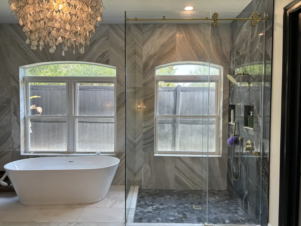 Wide view of a luxury master bathroom with a freestanding tub, chandelier and glass shower