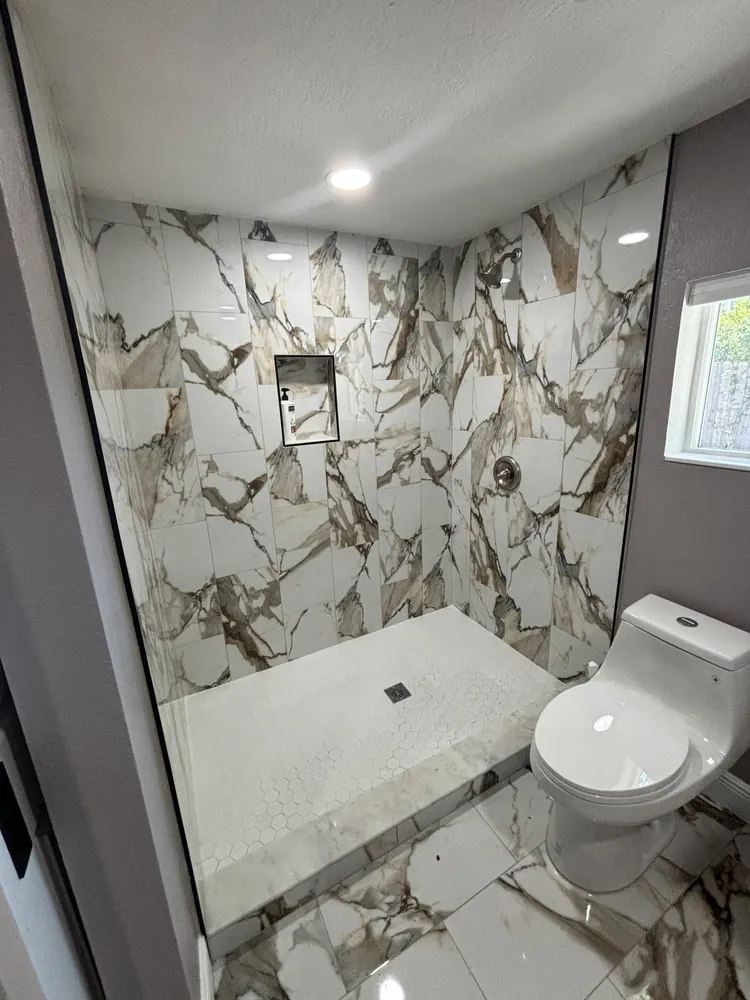 Shower with gold-veined marble-look tile and black trim in a remodeled bathroom