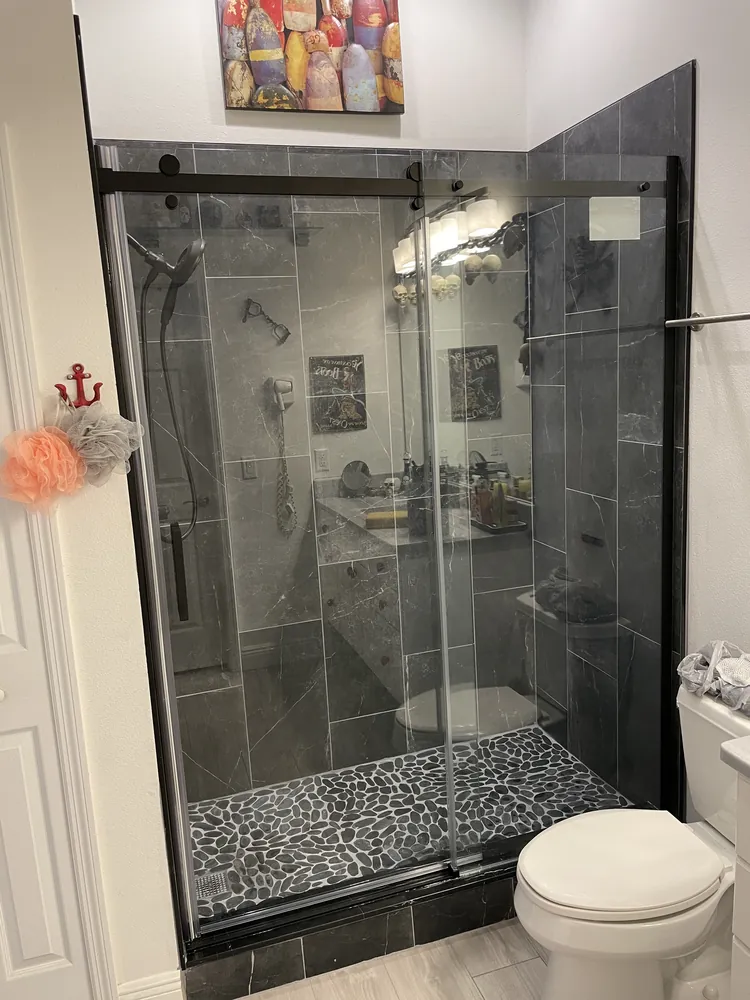 Shower with dark grey tile, a sliding glass door and a pebble floor