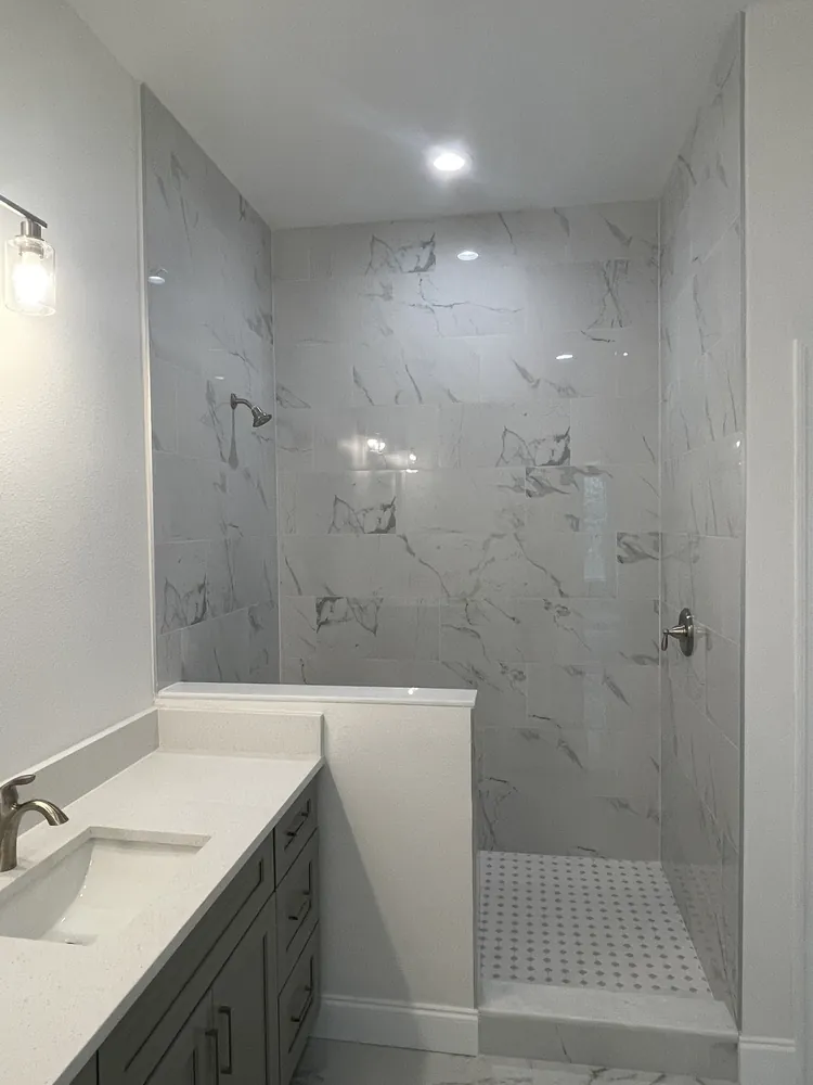 Bathroom with a grey vanity, white quartz top and a marble-look tiled shower