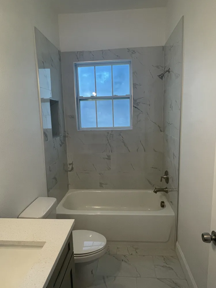 Tub and shower with marble-look tile and a window in a remodeled bathroom