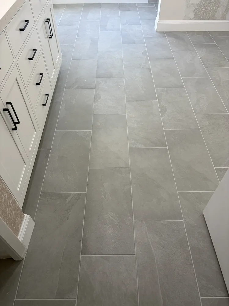 Large-format grey porcelain floor tile with a staggered layout beside a white vanity