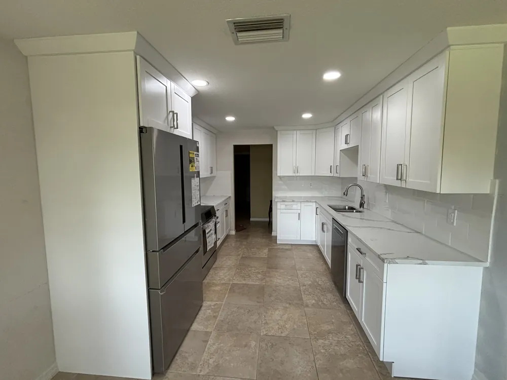 Galley kitchen with white shaker cabinets, quartz counters, stainless appliances and tile floor