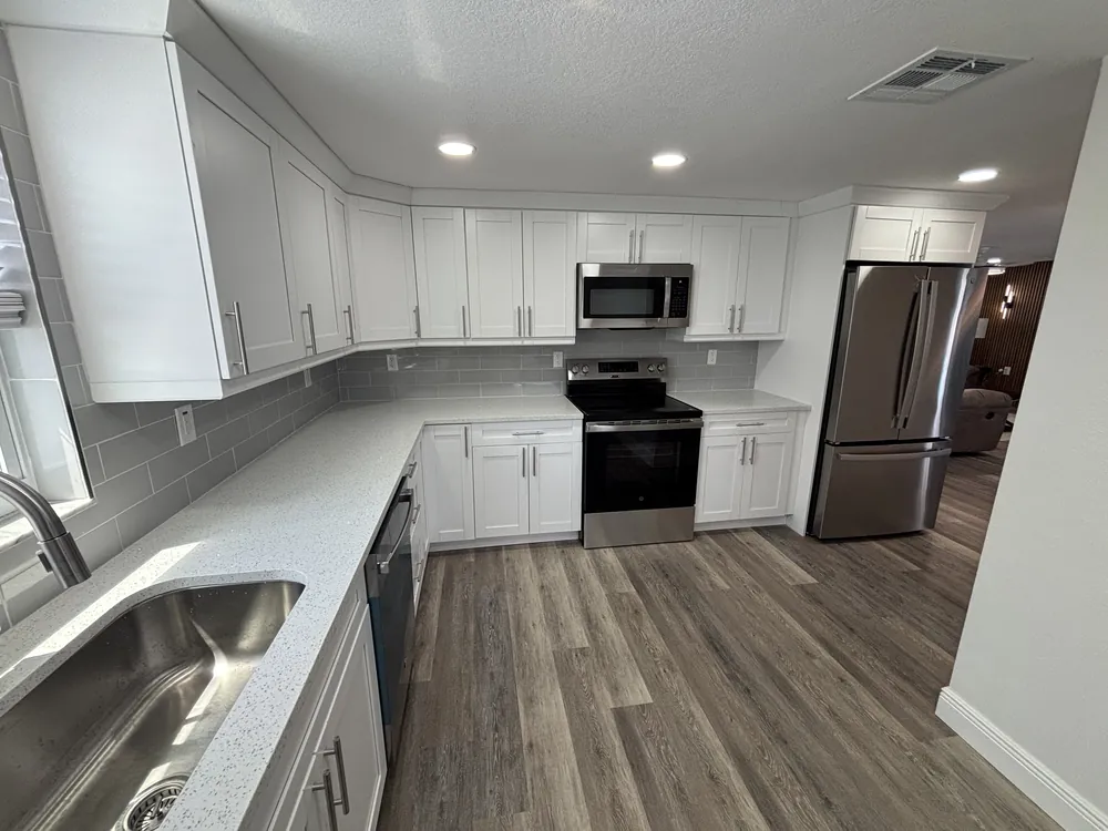 White shaker kitchen with stainless appliances and grey wood-look plank flooring