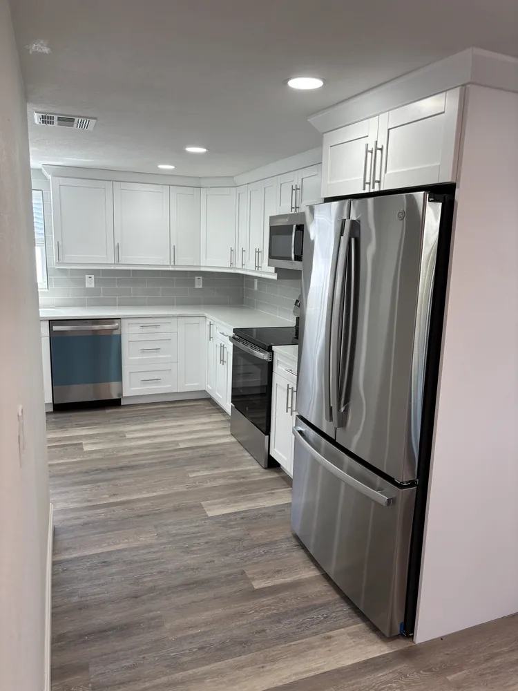 Remodeled kitchen with white cabinets, a stainless French-door refrigerator and grey plank floor