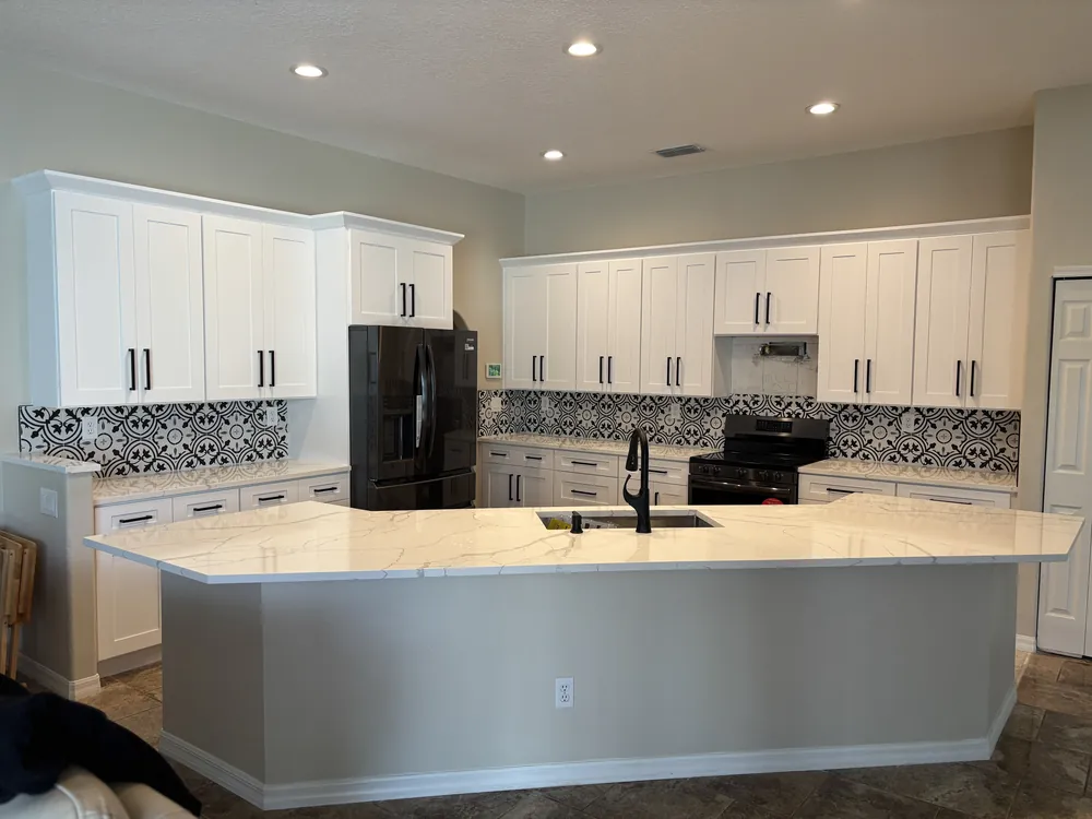 Kitchen with a large white island, patterned tile backsplash and black appliances